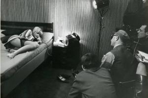 Sul set del film "Don Giovanni in Sicilia" - Regia Alberto Lattuada, 1967 - Totale. A sinistra, Ewa Aulin, sdraiata a letto su un fianco e con le gambe ranicchiate, parla al telefono. A destra, Alberto Lattuada e la troupe.