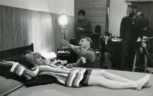 Sul set del film "Don Giovanni in Sicilia" - Regia Alberto Lattuada, 1967 - Ewa Aulin, sdraiata supina sul letto, tiene la cornetta del telefono all'orecchio e sorride a Lattuada accovacciato al suo fianco. Sullo sfondo membri della troupe.