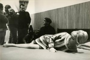 Sul set del film "Don Giovanni in Sicilia" - Regia Alberto Lattuada, 1967 - Ewa Aulin sdraiata prona su un letto, solleva le spalle appoggiando una mano al materasso. Sullo sfondo, membri della troupe.