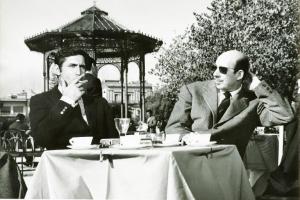 Scena del film "Don Giovanni in Sicilia" - Regia Alberto Lattuada, 1967 - Mezza figura di fronte di Lando Buzzanca, seduto al tavolo di un bar all'aperto, mentre aspira da una sigaretta. Seduto a destra, un uomo con gli occhiali da sole.