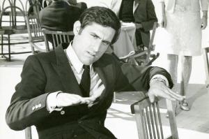 Scena del film "Don Giovanni in Sicilia" - Regia Alberto Lattuada, 1967 - Mezza figura frontale di Lando Buzzanca, seduto. L'attore tiene le mani a mezz'aria con i palmi rivolti verso il basso, in un gesto di invito alla calma, e la testa inclinata.