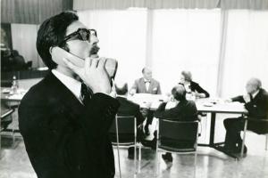 Scena del film "Don Giovanni in Sicilia" - Regia Alberto Lattuada, 1967 - Mezza figura di profilo di Lando Buzzanza al telefono. Sullo sfondo delle persone siedono a un tavolo riunioni.