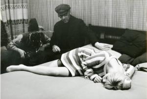 Sul set del film "Don Giovanni in Sicilia" - Regia Alberto Lattuada, 1967 - Ewa Aulin, sdraiata su un fianco, di traverso al letto. Sullo sfondo, Alberto Lattuada seduto dietro la macchina da presa e un altro membro della troupe.