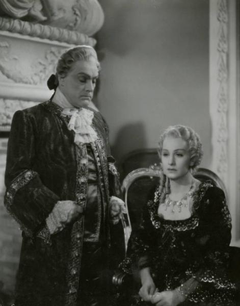 Scena del film "Le due orfanelle" - Regia Carmine Gallone, 1942 - Memo Benassi, in piedi, accanto a Tina Lattanzi. L'attore guarda verso il basso mentre l'attrice guarda dritto davanti a sé.
