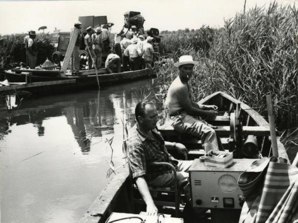 Sul set del film "Un ettaro di cielo" - Regia Aglauco Casadio, 1958 - A destra, in primo piano, ci sono due operatori seduti in barca, uno di essi maneggia un'asta. Sullo sfondo un gruppo di operatori su un altra barca sistemano la macchina da presa.