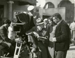 Sul set del film "I due sergenti" - Regia Enrico Guazzoni, 1936 - Il regista Enrico Guazzoni, al centro, seduto al lato della macchina da presa, dà indicazioni a Evi Maltagliati, al centro, e Gino Cervi, a destra.