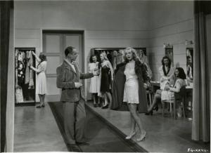 Scena del film "È caduta una donna" - Regia Alfredo Guarini, 1941 - A sinistra, un attore non identificato osserva un'attrice non identificata, a destra, che sta indossando una pelliccia. In secondo piano, attrici non identificate.