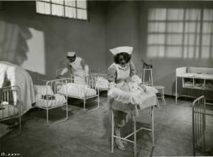Scena del film "È caduta una donna" - Regia Alfredo Guarini, 1941 - Totale di una stanza di ospedale in cui due attrici e un attore non identificati recitano nei panni di infermiere e medico.