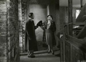 Scena del film "È caduta una donna" - Regia Alfredo Guarini, 1941 - Figure intere di Rossano Brazzi, a sinistra, con il cappello nella mano, e Isa Miranda, a destra, con la mano destra poggiata al fianco mentre si osservano sorridenti.