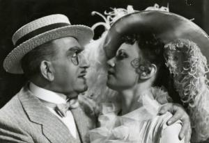 Scena del film "È tornato Carnevale" - Regia Raffaello Matarazzo, 1937 - Primo piano di Armando Falconi che abbraccia un'attrice non identificata con un cappello a tesa larga ornato di piume.