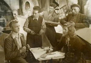 Scena del film "L'ebbrezza del cielo" - Regia Giorgio Ferroni, 1940 - Paolo Ketoff, seduto a sinistra, guarda a destra. Silvana Jachino, Mario Giannini, in piedi a sinistra, Franco Brambilla, al suo fianco, e un attore non identificato, lo osservano.