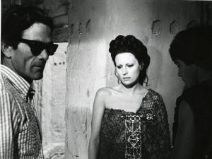 Sul set del film "Edipo Re" - Regia Pier Paolo Pasolini, 1967 - A sinistra, Pier Paolo Pasolini, indossa occhiali da sole e rivolge lo sguardo a destra. Silvana Mangano, al centro, e Franco Citti, a destra, osservano in basso a sinistra.