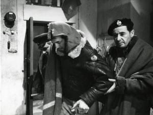 Scena del film "Era notte a Roma" - Regia Roberto Rossellini, 1960 - Peter Baldwin, al centro con in mano una bottiglia, si dirige verso sinistra, sostenuto da Leon Genn, a destra e Serghej Bondarciuk, a sinistra in secondo piano.