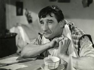 Scena del film "L'eroe sono io" - Regia Carlo Ludovico Bragaglia, 1951 - Renato Rascel, seduto con i gomiti poggiati a un tavolo e un tovagliolo a mo' di bavaglia, osserva verso sinistra.