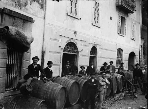 Piazza Brembana. Travaso del vino dalle botti davanti al negozio di generi diversi, vini e liquori gestito da Ferdinando Calegari
