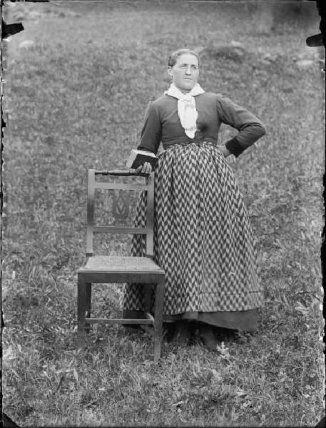 Val Brembana. Ritratto di donna appoggiata a una sedia con libro in mano in un prato