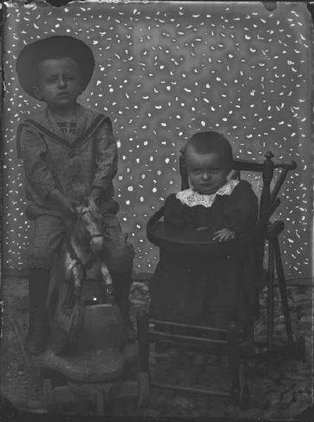 Val Brembana. Ritratto di due bambini seduti su un cavallo a dondolo e su un seggiolino