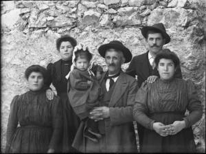 Val Brembana. Ritratto di famiglia con bambina in braccio al nonno al centro. Casa rurale sullo sfondo