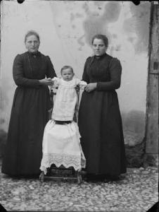 Val Brembana. Ritratto di due donne con un bambino in piedi sul seggiolone