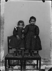 Val Brembana. Ritratto di due bambine che si tengono per mano in piedi su sedie