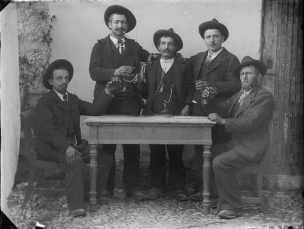 Val Brembana. Ritratto di gruppo di uomini attorno a un tavolo in atto di brindare