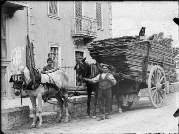 Piazza Brembana. Trasporto di legname segato su carro trainato da cavalli in via Bortolo Belotti