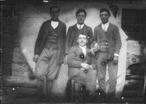 Val Brembana. Ritratto di quattro giovani uomini con casa rurale sullo sfondo