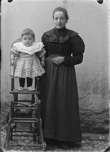 Val Brembana. Ritratto di donna con bambino in piedi sul seggiolone