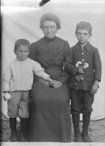 Val Brembana. Ritratto di donna con due bambini che tengono fiori in mano