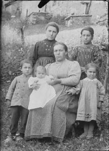 Val Brembana. Ritratto di donna con ragazzine e bambini in un prato davanti a una casa rurale