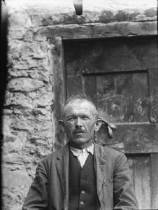 Val Brembana. Ritratto di uomo anziano davanti alla porta di una casa rurale