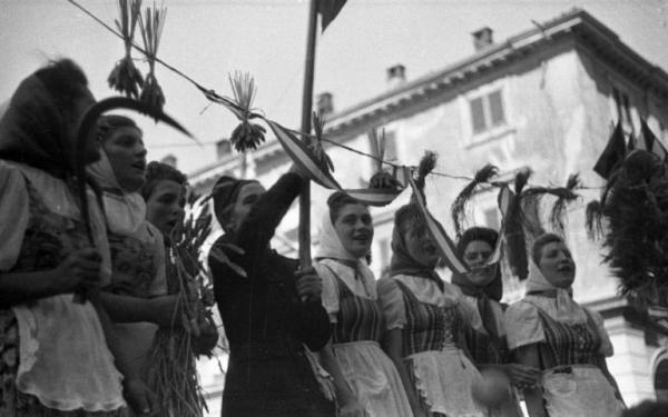 Ritratto di gruppo femminile - Otto donne intonano un coro, una donna tiene la falce in mano - Garlasco - Festa delle mondine - Scorcio di un palazzo sullo sfondo