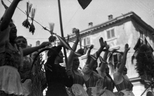 Ritratto di gruppo femminile - Otto donne con il braccio destro alzato - Garlasco - Festa delle mondine - Scorcio di un palazzo