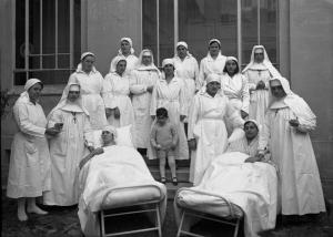 Ritratto di gruppo - Infermiere religiose e civili, con bambino e due degenti distese sul letto - Pavia - Ospedale Policlinico San Matteo
