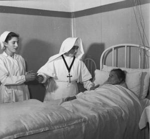 Pavia - Piazza XXV maggio - Casa di cura «E. Morelli» - Infermiera assistente porge il termometro all'infermiera religiosa - Paziente distesa a letto