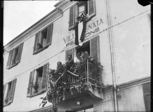 Salice Terme - IX Festa nazionale dell'uva - Gruppo di persone si affaccia dal balcone e dalle finestre di un palazzo adibito a pensione - Grappoli d'uva e tralci decorano il balcone