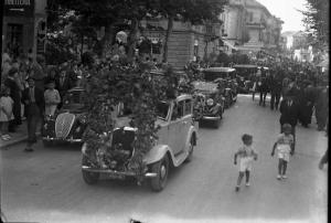 Salice Terme - IX Festa nazionale dell'uva - Sfilata di un'autovettura addobbata con tralci e grappoli d'uva, seguita da altre vetture - Folla di persone - Due bambini a destra dell'immagine