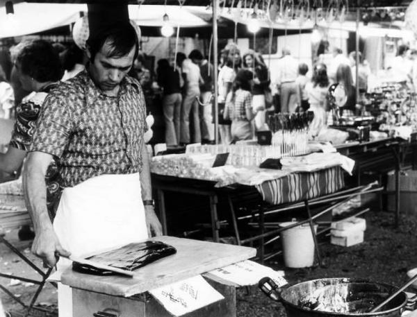 La sagra. Preparazione della 'tiraca'. Uomo che cucina dietro ad un bancone di vendita di dolci.