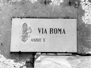 Via Roma, anno X. Targa in marmo con "via Roma/anno X" e fascio littorio.