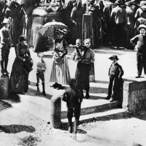 Personaggi attorno al monumento a Tommaso Grossi. Donne e bambini nella piazza assolata.