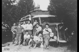 Emigranti valdimagnini  in posa attorno ad un camion carico di tronchi. Bosco ai lati e sullo sfondo. Il 3° da sinistra,  inginocchiato, è Francesco Facchinetti.