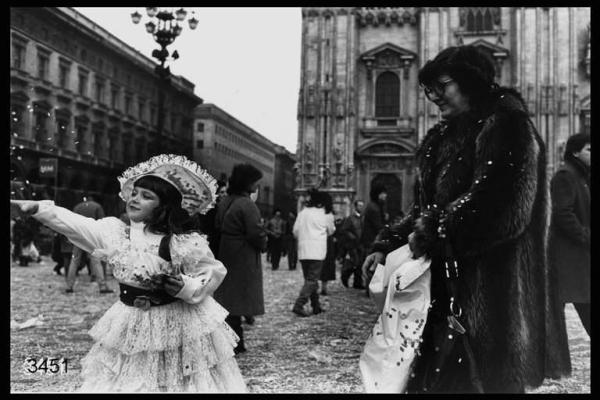 Carnevale ambrosiano. Piazza Duomo: in primo piano signora in pelliccia e bambina in costume.