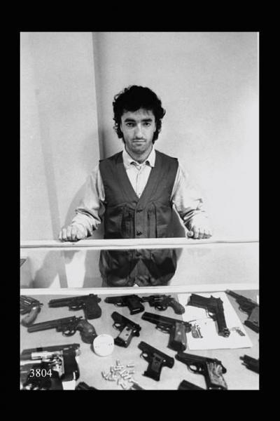 Fabbrica armi. Uomo davanti a una bacheca con pistole e revolver.