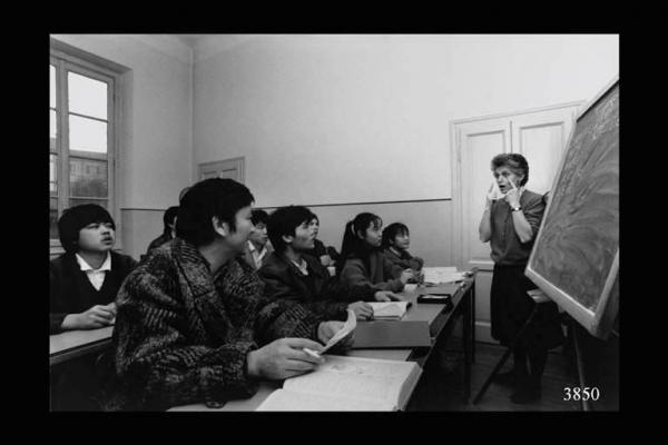 Corso di italiano per lavoratori cinesi.  Insegnante di fianco a una lavagna, parla a un gruppo di allievi. Immigrazione cinese.