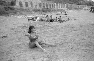 Rodi Garganico. Spiaggia. Set del film "La legge", diretto da Jules Dassin. Gina Lollobrigida, seduta sulla sabbia, si prepara a lanciare sassi nel mare