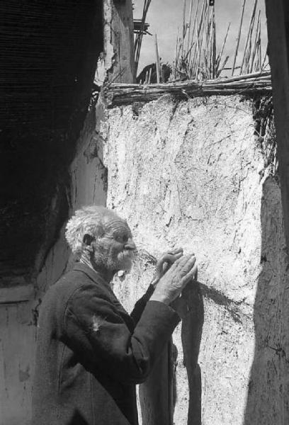 Località non identificata.Terremoto. Uomo anziano tocca, con le mani, la parete di una casa distrutta dal sisma