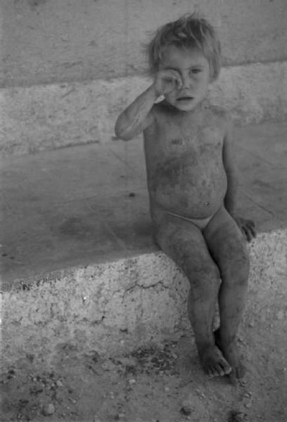 Cassino. Bambina nuda seduta sul marciapiede