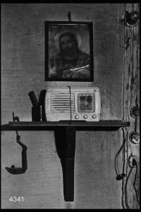 Interno di abitazione. Radio su una mensola sovrastata da immagine religiosa.
