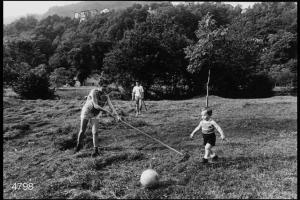 Raccolta del fieno. Una donna e un ragazzo raccolgono il fieno, un bambino gioca a palla.