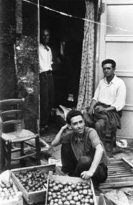 Baracche. Tre uomini all'ingresso di una baracca con cassette di pomodori.